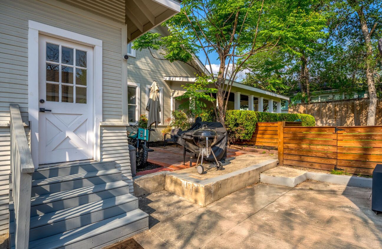 A house with a covered porch, a barbecue grill, and a wooden fence.