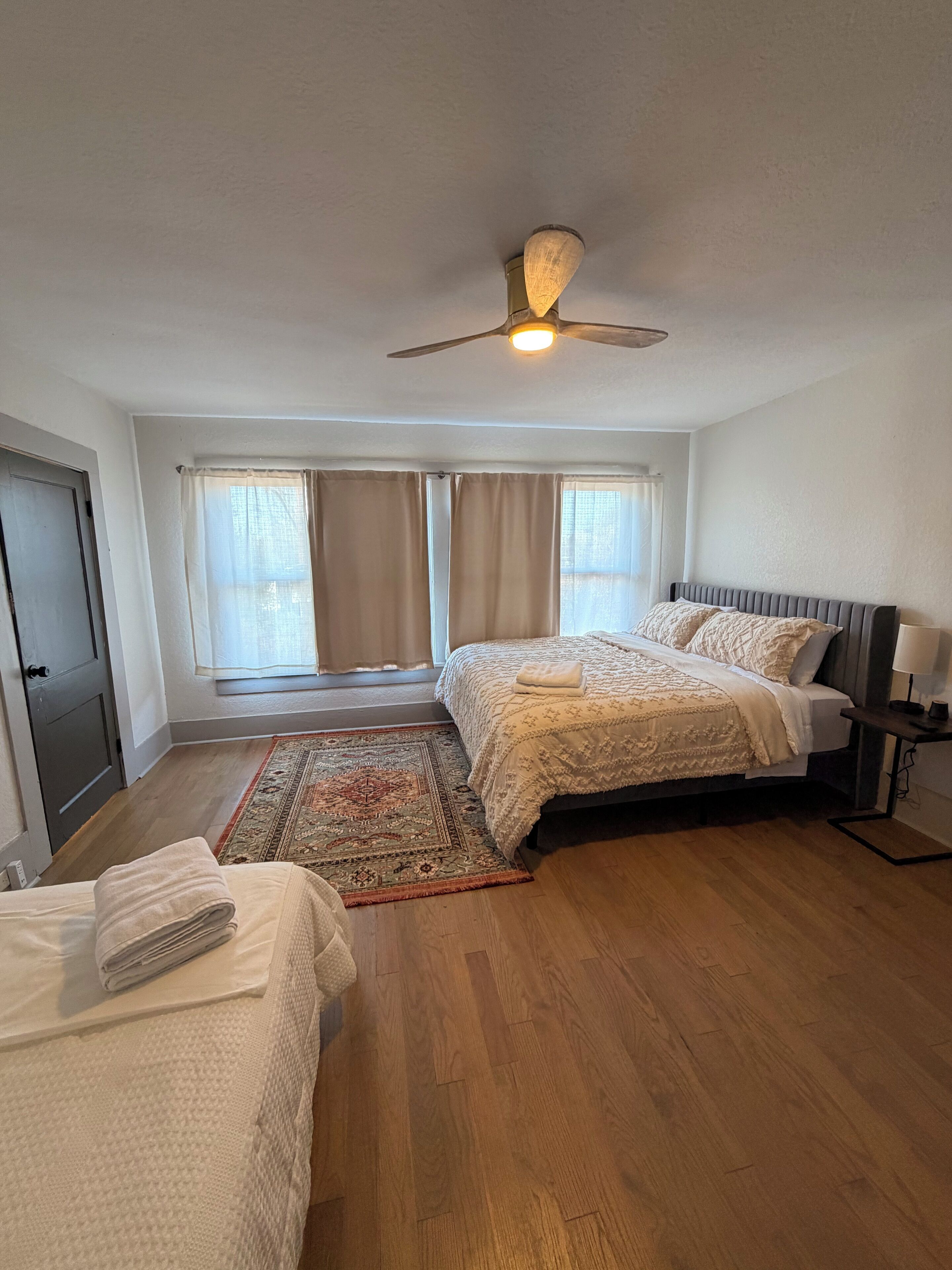 A bedroom with two beds, a ceiling fan, a rug, and a window with curtains.