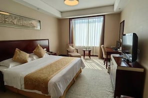 Habitación de hotel con una cama grande, un escritorio, una silla, un televisor y una ventana con cortinas.