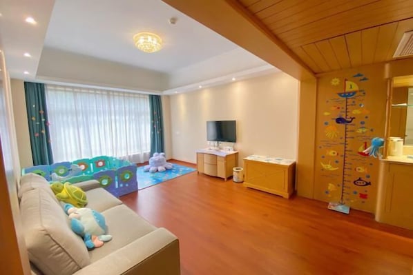A living room with a sofa, a TV, a play area with toys, and a wooden cabinet. - Xikang Hotel (Nanjing)