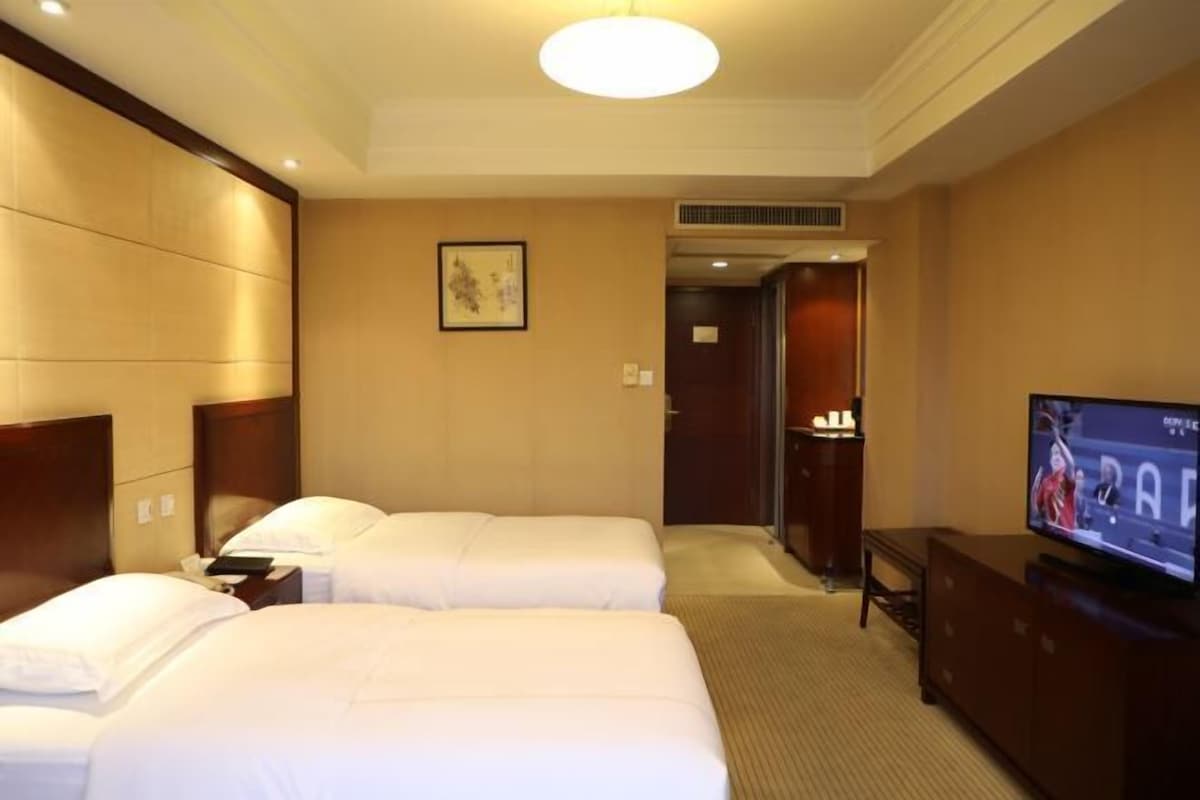 A hotel room with two beds, a television, a desk, and a door leading to a bathroom.