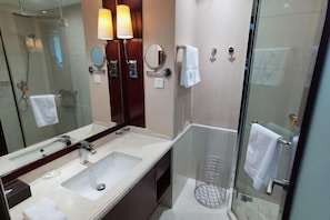 A modern bathroom with a large mirror, two wall-mounted lights, a sink, and a glass shower enclosure. - Xikang Hotel (Nanjing)