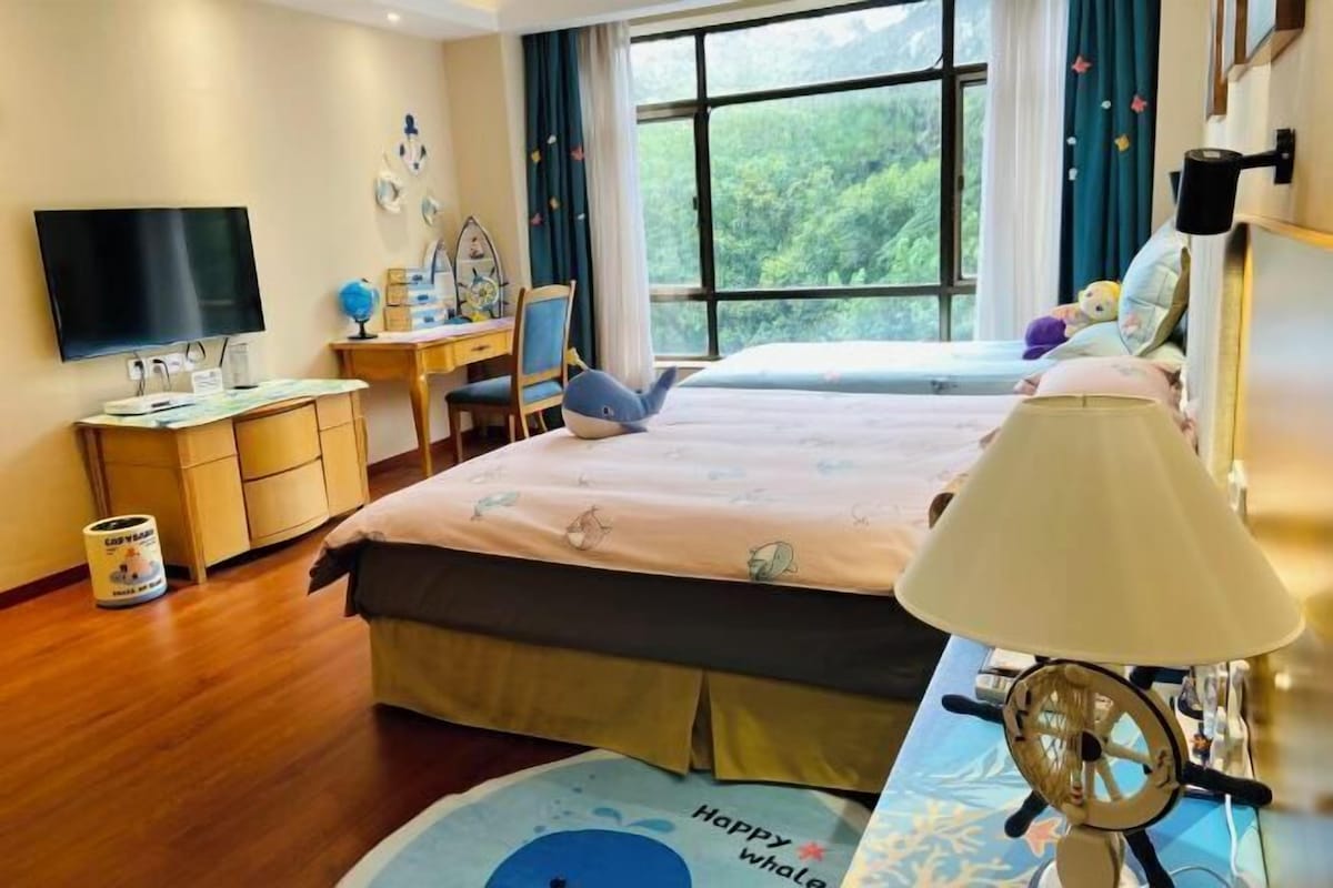 A hotel room with a bed, a desk, a TV, and a window with a view of trees.