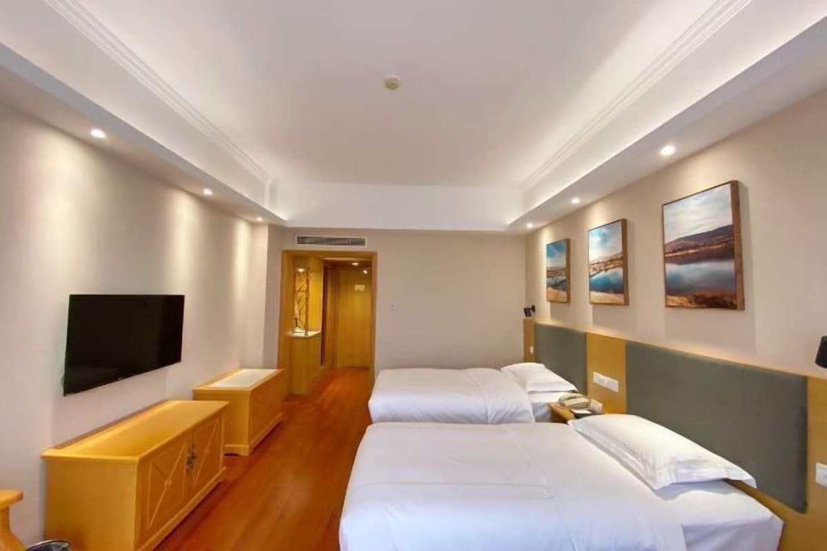 A hotel room with two beds, a TV, a wooden cabinet, and artwork on the walls.