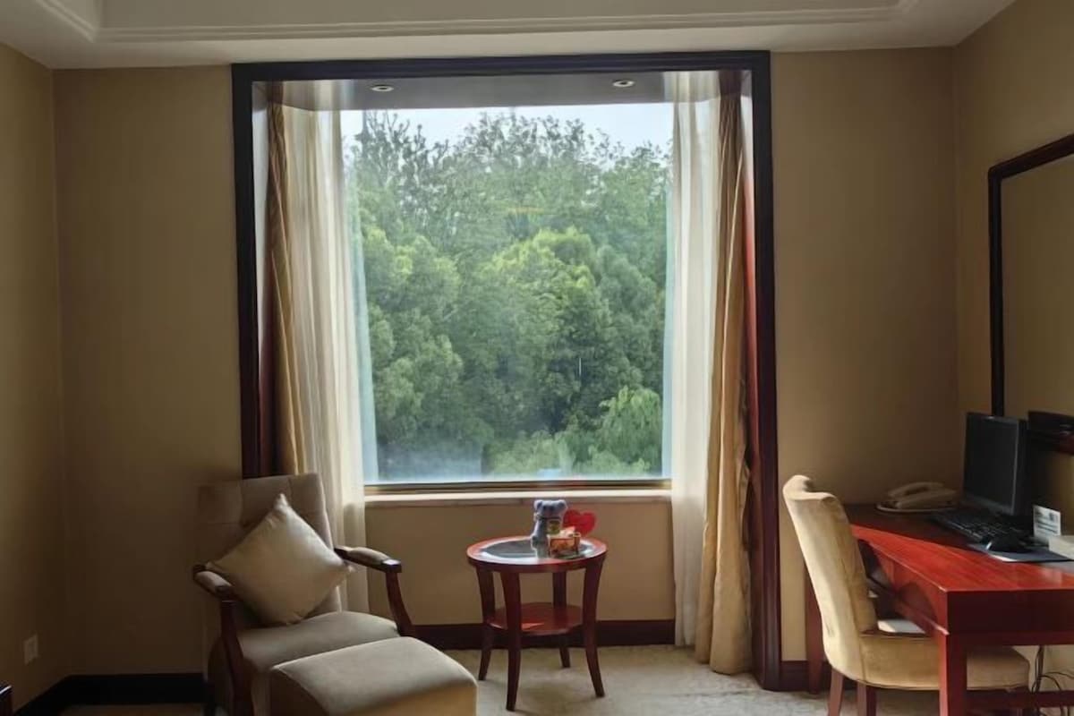 A room with a large window, a desk with a computer, a chair, and a small table with decorative items.