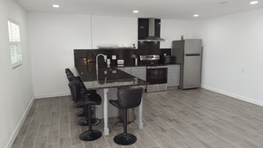 A modern kitchen with a black countertop, stainless steel appliances, and a bar stool area. - Boutique Beach Escape in Indian Rocks Beach - 150 steps to the sand (Indian Rocks Beach)