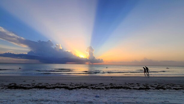 A beach scene with a sunset, calm sea, and two people walking on the shore. - Boutique Beach Escape in Indian Rocks Beach - 150 steps to the sand (Indian Rocks Beach)
