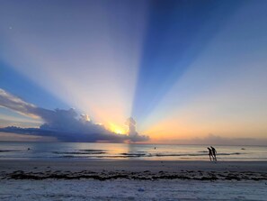 A beach scene with a sunset, calm sea, and two people walking on the shore. - Boutique Beach Escape in Indian Rocks Beach - 150 steps to the sand (Indian Rocks Beach)