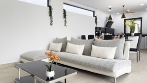 A modern living room with a sofa, a glass coffee table, and a kitchen area in the background. - Stylish 3BR Pool Villa Lawan Villa (LWV1) (Chalong)