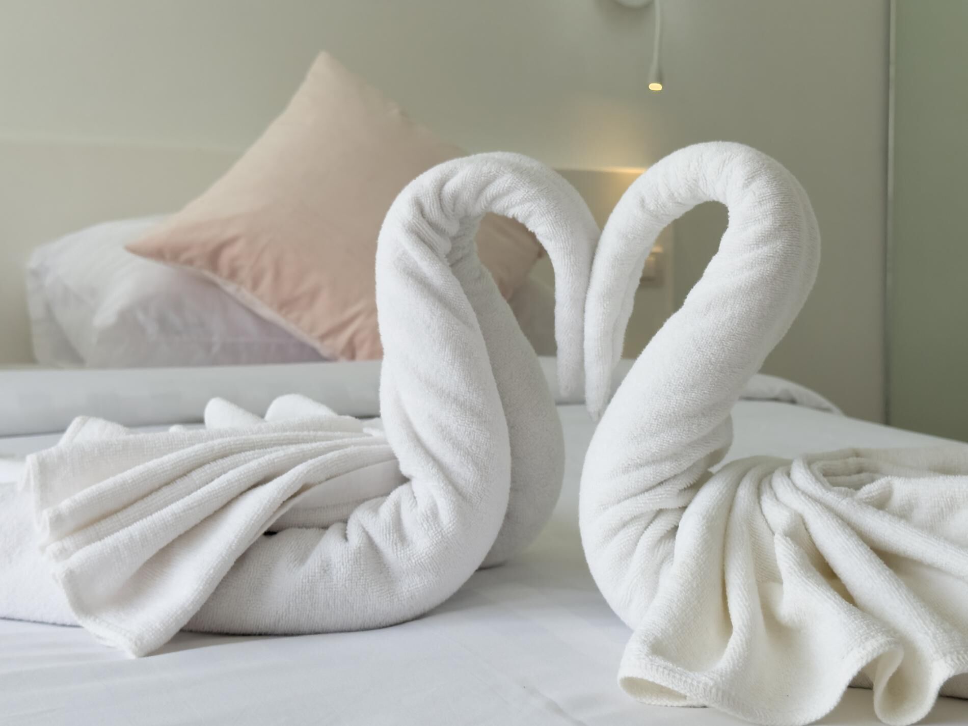 Ein ordentlich bezogenes Bett mit zwei weißen Handtüchern, die zu Schwänen geformt sind.