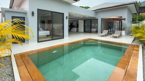 A modern house with a swimming pool, large glass doors, and a patio area with lounge chairs. - Stylish 3BR Pool Villa Lawan Villa (LWV1) (Chalong)