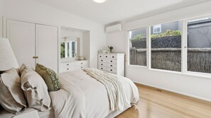 Un dormitorio con cama, cómoda, espejo y ventana con vistas a una valla y follaje.