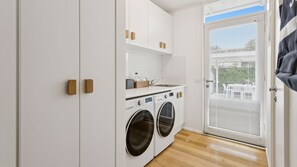 Une petite buanderie comprenant un lave-linge, un évier et un petit plan de travail sur lequel sont posées des bouteilles.