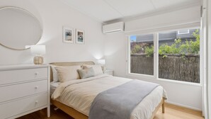 A bedroom with a bed, bedside tables, a dresser, a mirror, and a window with a view of a fence and greenery. - La Plage Portsea Escape with Pool (Portsea)