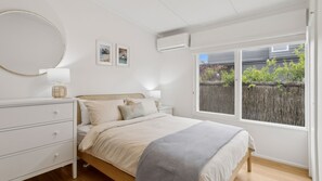 A bedroom with a bed, bedside tables, a dresser, a mirror, and a window with a view of a fence and greenery. - La Plage Portsea Escape with Pool (Portsea)