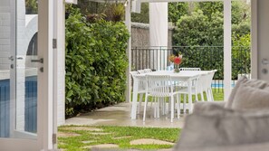 An outdoor patio with a white table and chairs, surrounded by greenery and a pool. - La Plage Portsea Escape with Pool (Portsea)