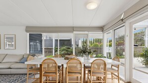 A dining area with a white table and rattan chairs, large windows, and a view of a garden. - La Plage Portsea Escape with Pool (Portsea)