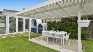 Un patio techado con mesa y sillas, una parrilla y una valla blanca.