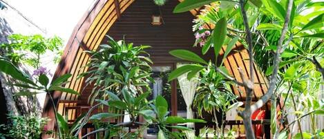 A wooden house with an arched roof surrounded by lush greenery.