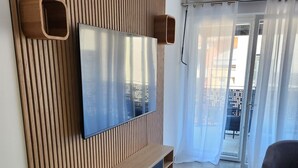A modern living room with a large flat-screen TV mounted on a wooden slatted wall, a sofa, two ottomans, and a patterned rug. - Upscale 2-bathroom apartment (Toulouse)