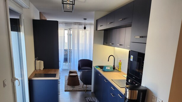 A modern kitchen with a built-in oven, a coffee maker, and a sink. There is a chair and a small table in the center of the room. - Upscale 2-bathroom apartment (Toulouse)