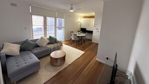 Un salon moderne avec un canapé gris, une table basse ronde et un coin repas comprenant une table et des chaises blanches.