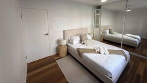 Une chambre à coucher avec un lit, des tables de chevet, un miroir et une porte.