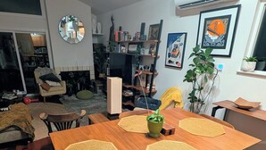Ein Essbereich mit einem Holztisch, gewebten Unterlagen und Stühlen. Ein Bücherregal mit verschiedenen Gegenständen und ein Spiegel an der Wand sind ebenfalls vorhanden.