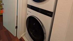 Eine gestapelte Waschmaschine und ein Trockner in einem Hauswirtschaftsraum mit Holzboden und weißer Tür.