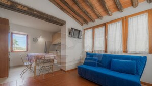 A room with a blue sofa, a dining table with chairs, a kitchen area, and a window with curtains. - IL BORGHETTO - BILOCALE IL BORGHETTO (Campo nell'Elba)