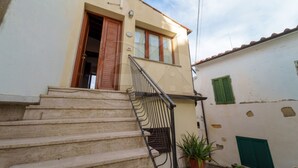 A building with a set of stone steps leading to a wooden door, a small potted plant, and a green shuttered window. - IL BORGHETTO - BILOCALE IL BORGHETTO (Campo nell'Elba)