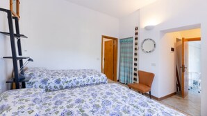 Quarto com duas camas, um arranhador para gatos, uma cadeira, um espelho e uma porta que dá para outro cômodo.