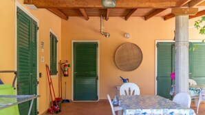 Une terrasse couverte avec une table et des chaises, un extincteur et une porte avec un volet vert.