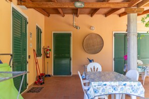 A covered patio with a table and chairs, a fire extinguisher, and a door with a green shutter.