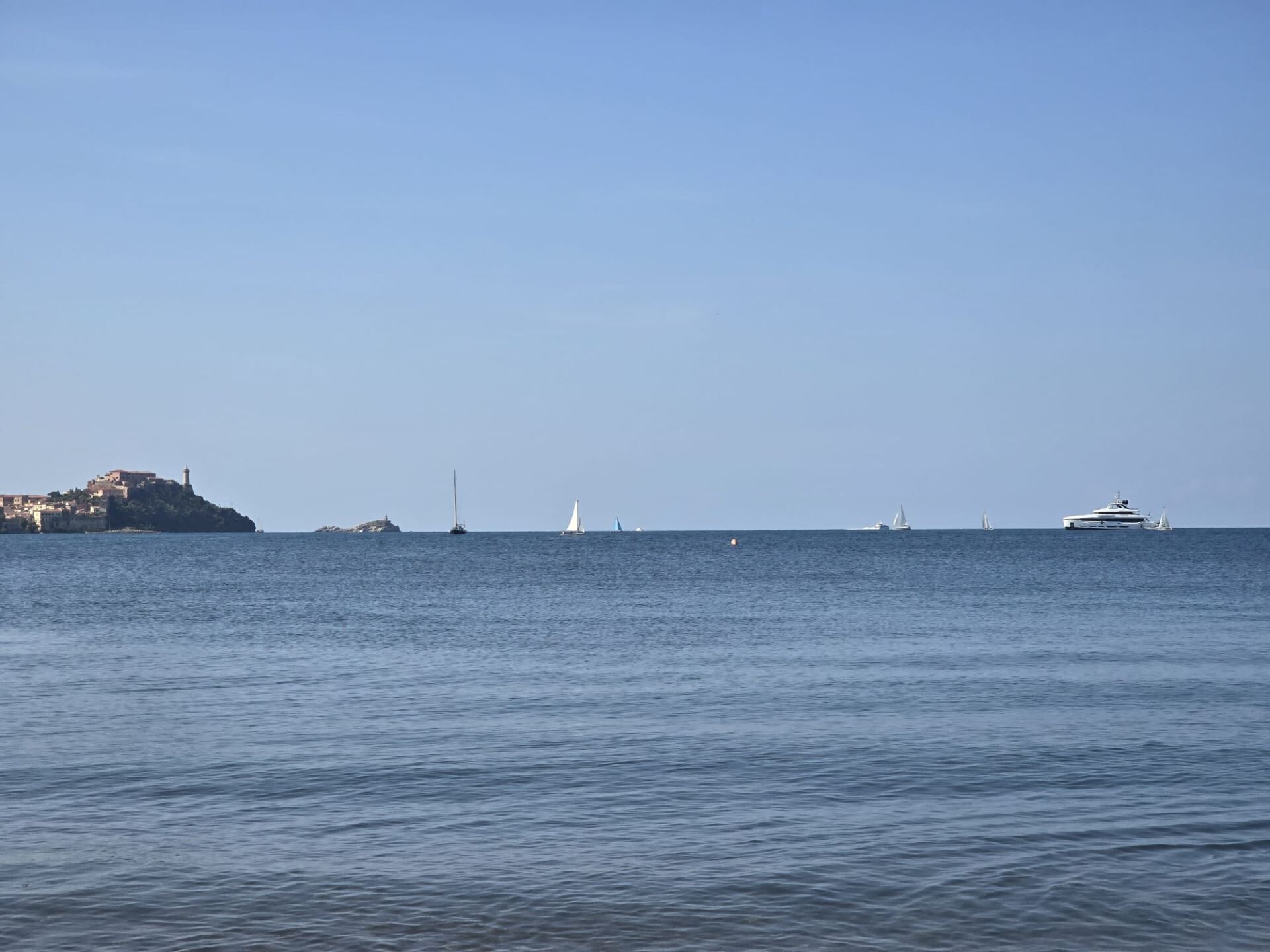 Blick auf die Küste mit einer kleinen Insel und mehreren Segelbooten.
