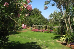 A garden with a grassy lawn, flowering plants, and a wooden pergola structure.