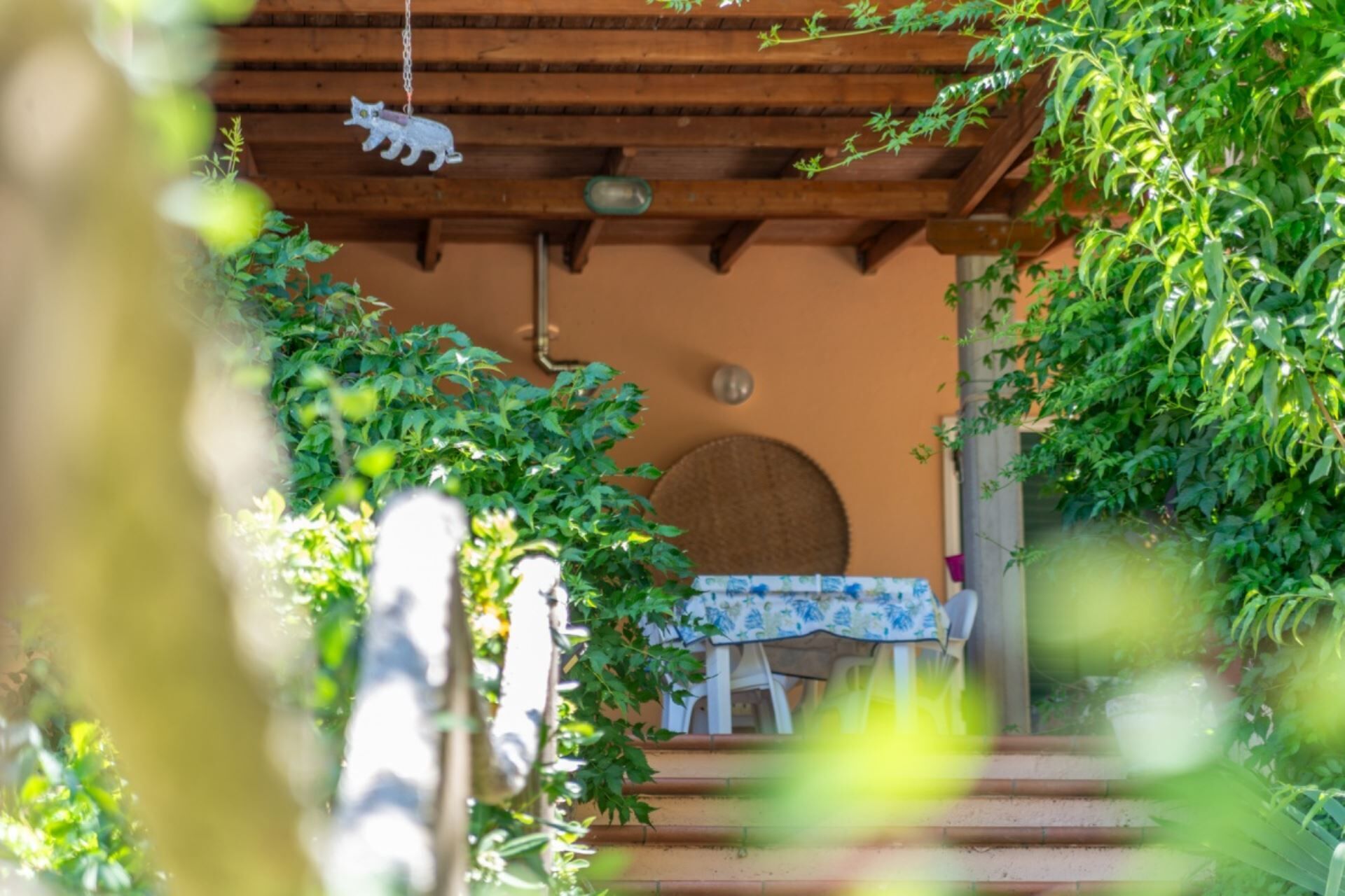 A wooden pergola with a hanging cat decoration, a round wall-mounted object, and a table with a patterned tablecloth.
