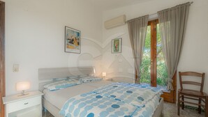 Un dormitorio con cama, mesitas de noche, una silla y una ventana con cortinas.