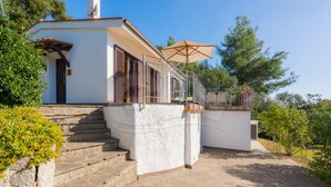 Un edificio blanco con una escalera de piedra que lleva a un balcón con una sombrilla color beige.