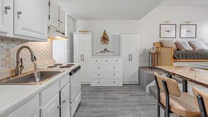 Cozinha compacta com armários brancos, fogão embutido e espaço de refeições com mesa e cadeiras.