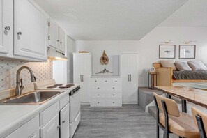 A compact kitchen with white cabinets, a built-in stove, and a dining area with a table and chairs. - Brookside II B-205 - Sunday River Slopeside Condominium (Newry)