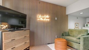 Uma sala de estar moderna com uma televisão de tela plana, um sofá verde, um armário de madeira e um letreiro de neon na parede.