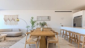 Ett modernt vardagsrum med ett matbord i trä, bekväma sittplatser, en soffa, ett soffbord, en golvlampa, en väggklocka och ett köksområde med ett kylskåp.