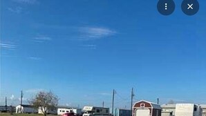 Paesaggio rurale con una strada sterrata, un fienile rosso e diversi camper parcheggiati sullo sfondo.