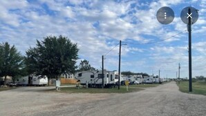 Una strada sterrata conduce a una fila di camper e roulotte, con pali dell'alta tensione e cielo sereno.