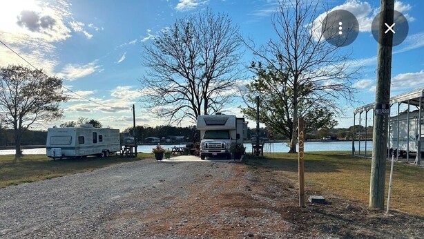 Un campeggio con camper parcheggiati vicino a un lago, un'area picnic coperta e un sentiero sterrato.