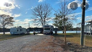 Un’area di parcheggio sterrata con camper e un’area picnic coperta vicino al lago.