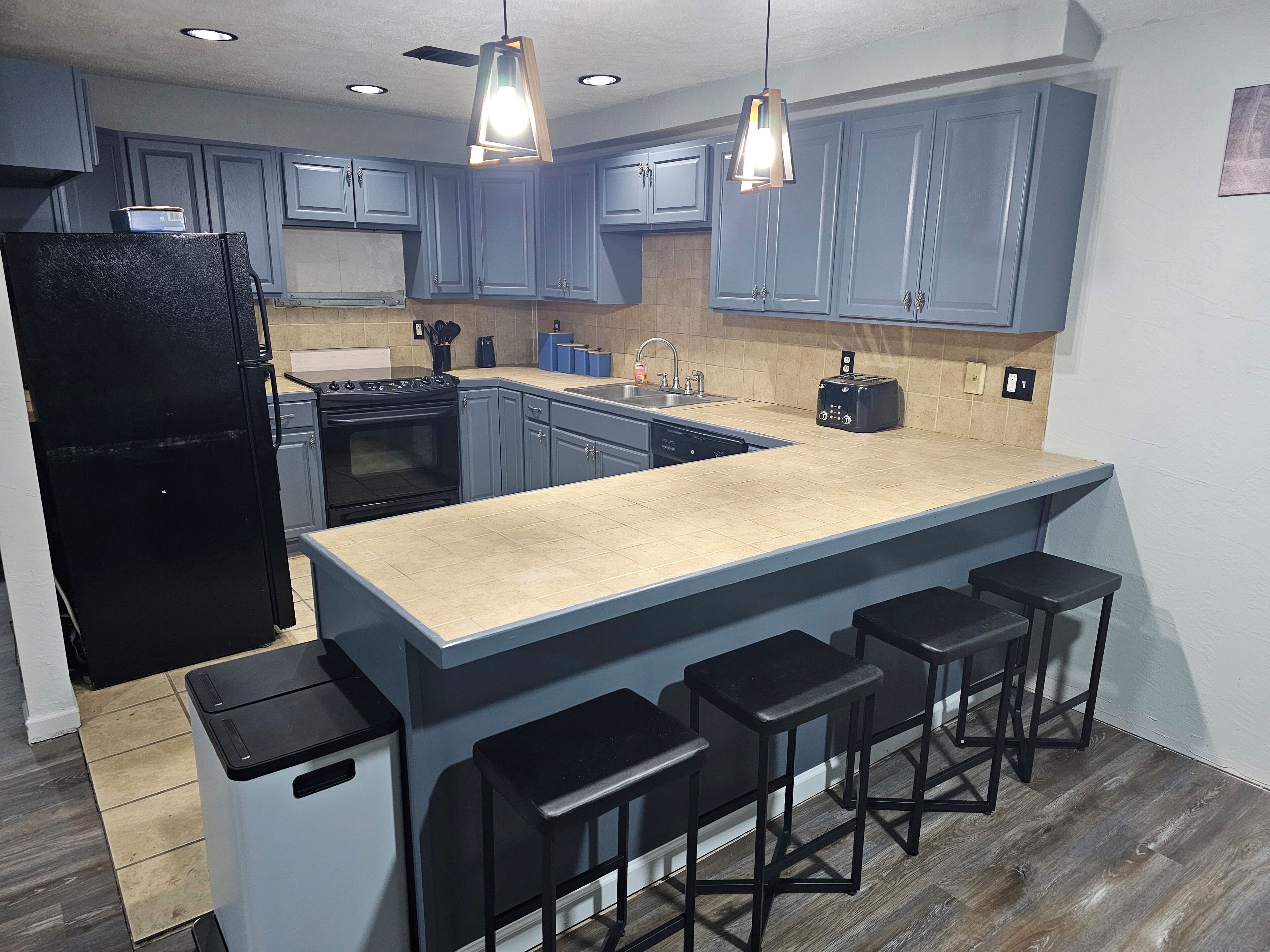 A modern kitchen with blue cabinets, a black refrigerator, a stove, and a large island with bar stools.