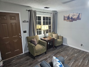 A living room with a brown door, two patterned armchairs, a small table with a lamp, and a window with curtains. - Outskirts of Gatlinburg, Minutes to everything 3-bedroom apartment in Gatlinburg (Gatlinburg)