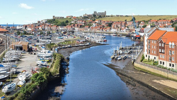 Ein Hafen mit Booten, eine Burg im Hintergrund und eine Stadt mit roten Dächern.
